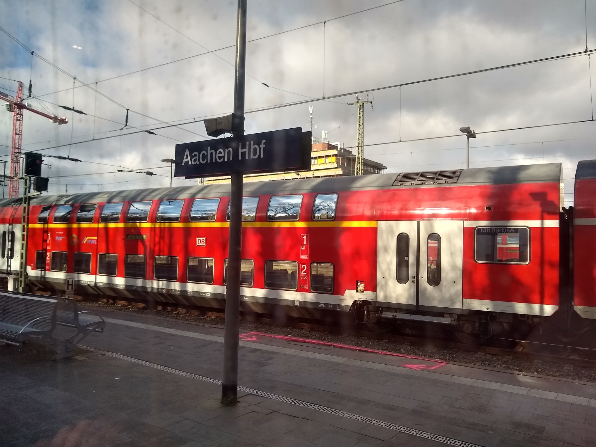 Platform sign saying Aachen Hbf with a double-decker red DB regional train